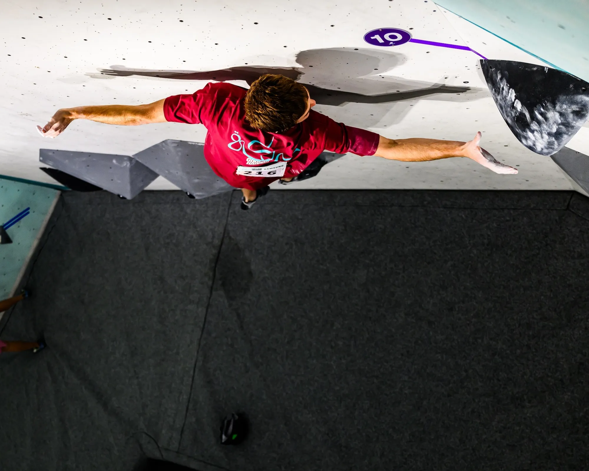 A competitor spanning wide across a grey volume, seen from above with the mats below