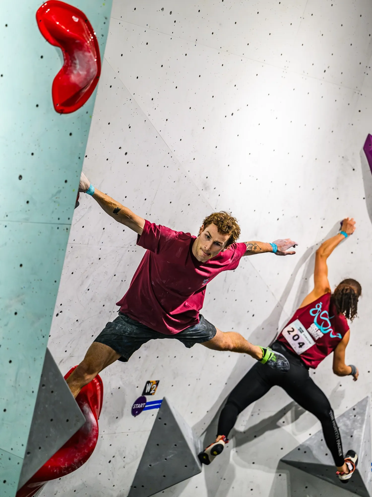 A competitor stretched between red holds on the steepest part of the wall