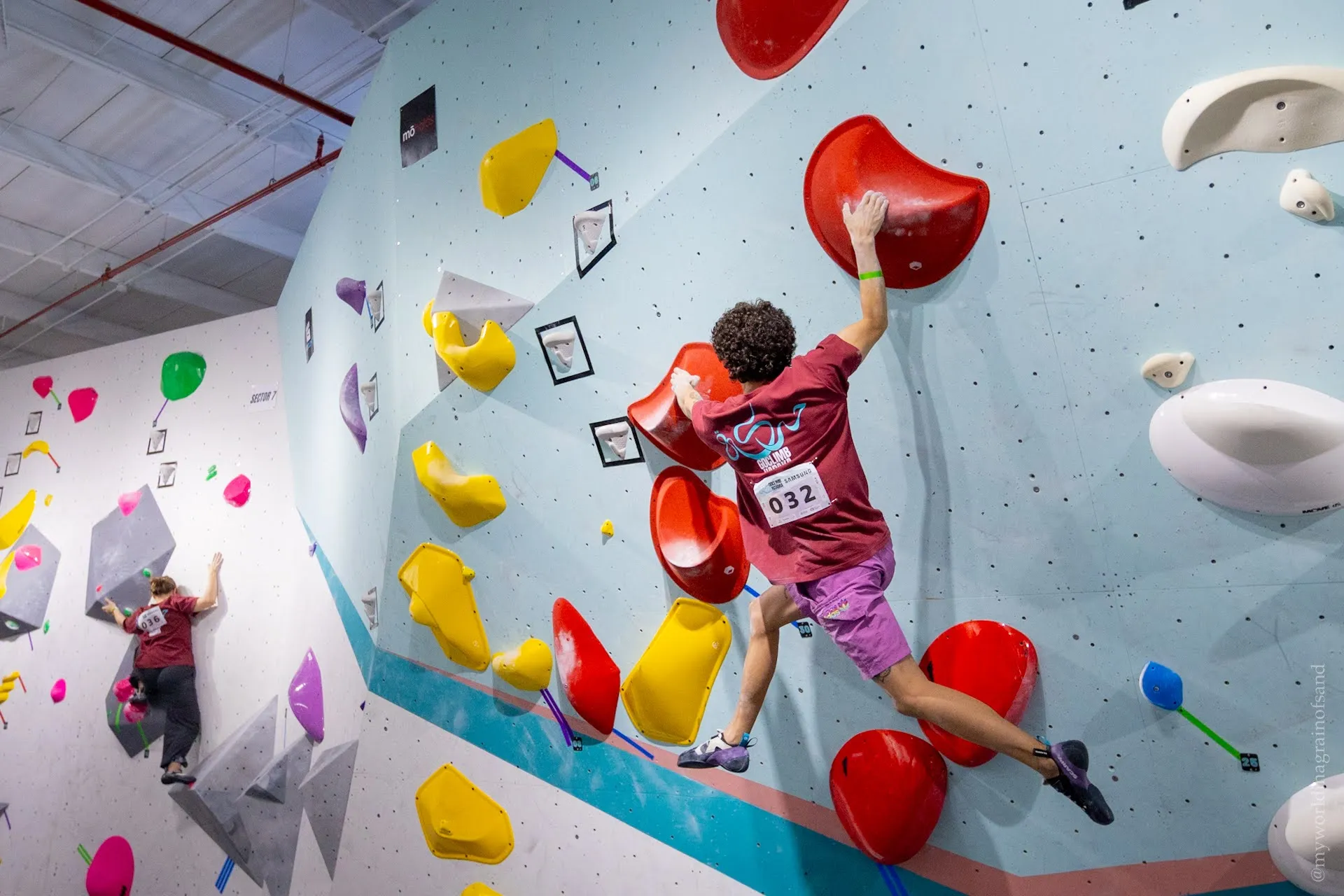 The competition wall seen from across the gym, a climber mid-route among the holds