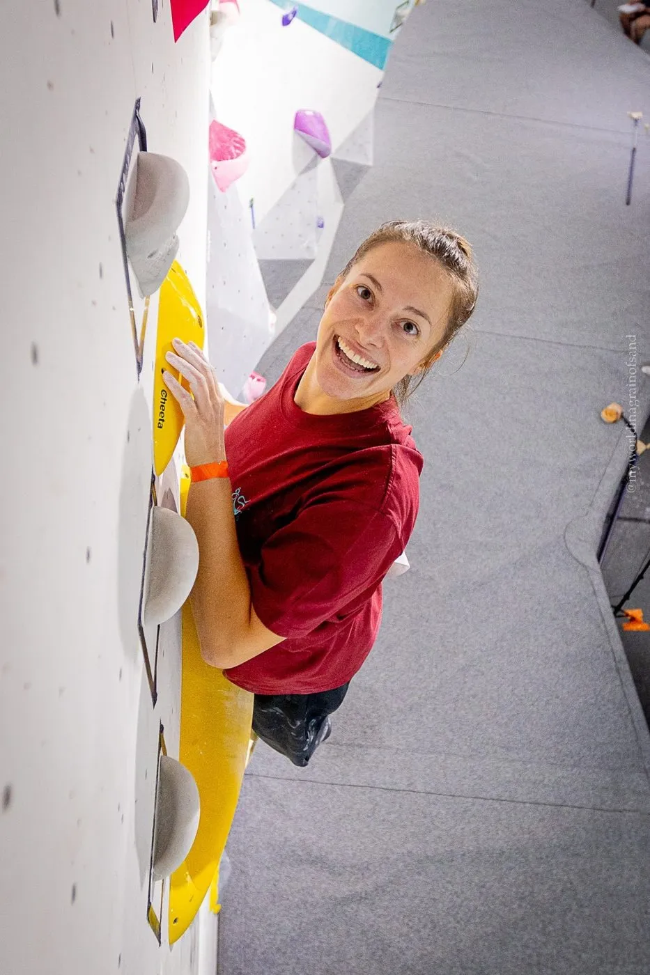 A climber grinning from halfway up the wall